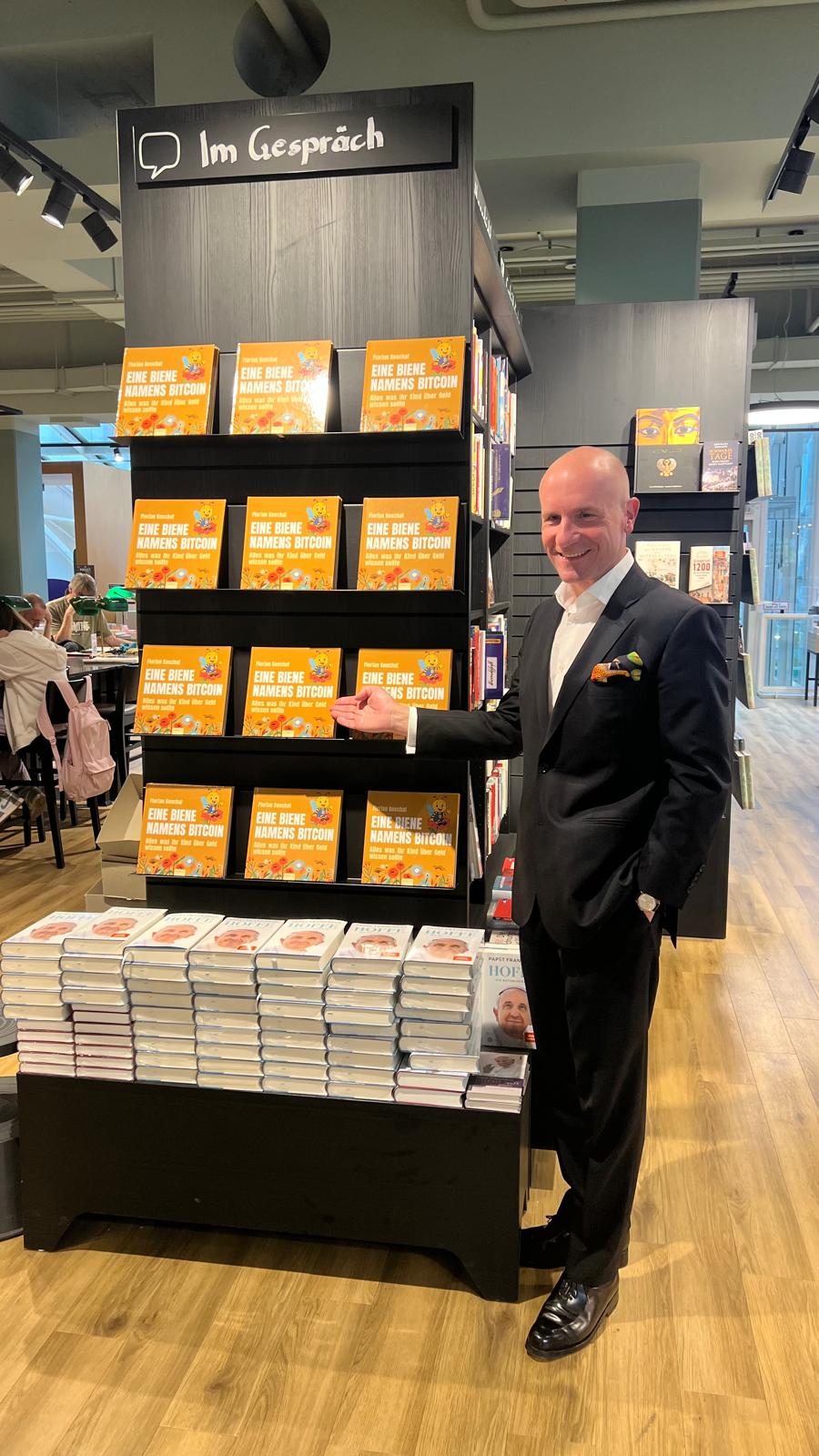 Dr. Florian Koschat im Buchhandel vor einem Regal mit „Eine Biene namens Bitcoin“